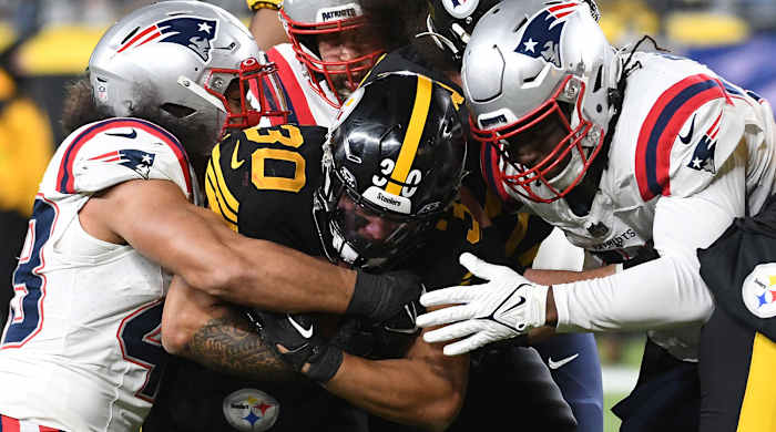 Jaylen Warren is wrapped up by three Patriots defenders while he clutches the ball tightly